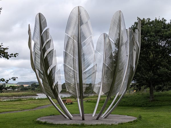 A steel sculpture of nine 20-foot high eagle feathers arranged in a circle set in park.